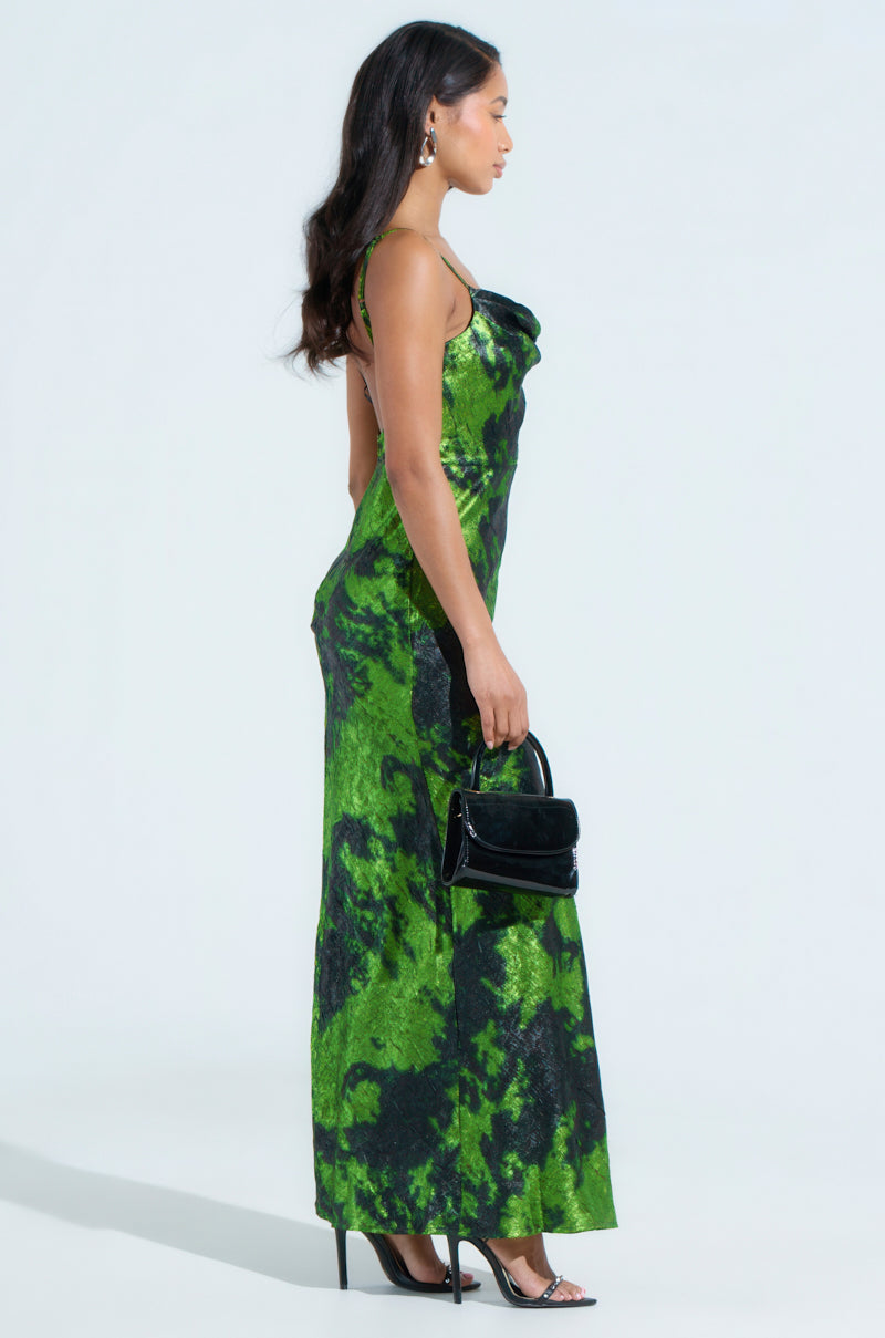 A woman in a LENNON PRINTED METALLIC MAXI DRESS poses in profile against a plain background. She carries a small black handbag and wears high heels, with her long hair flowing down her back.