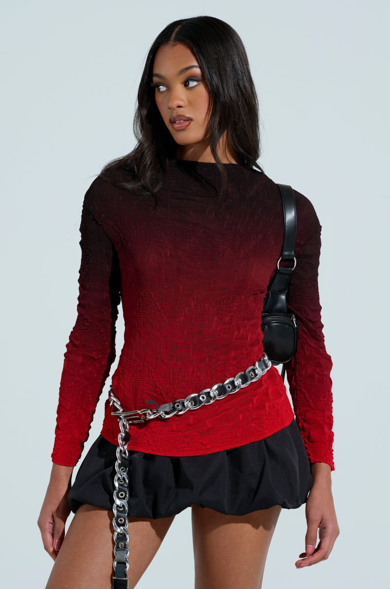 A person with long hair wears the BURNING PASSION TOP, featuring a red-to-black ombre design, paired with a short black skirt, silver chain belt, and a small black shoulder bag against a plain light gray background.