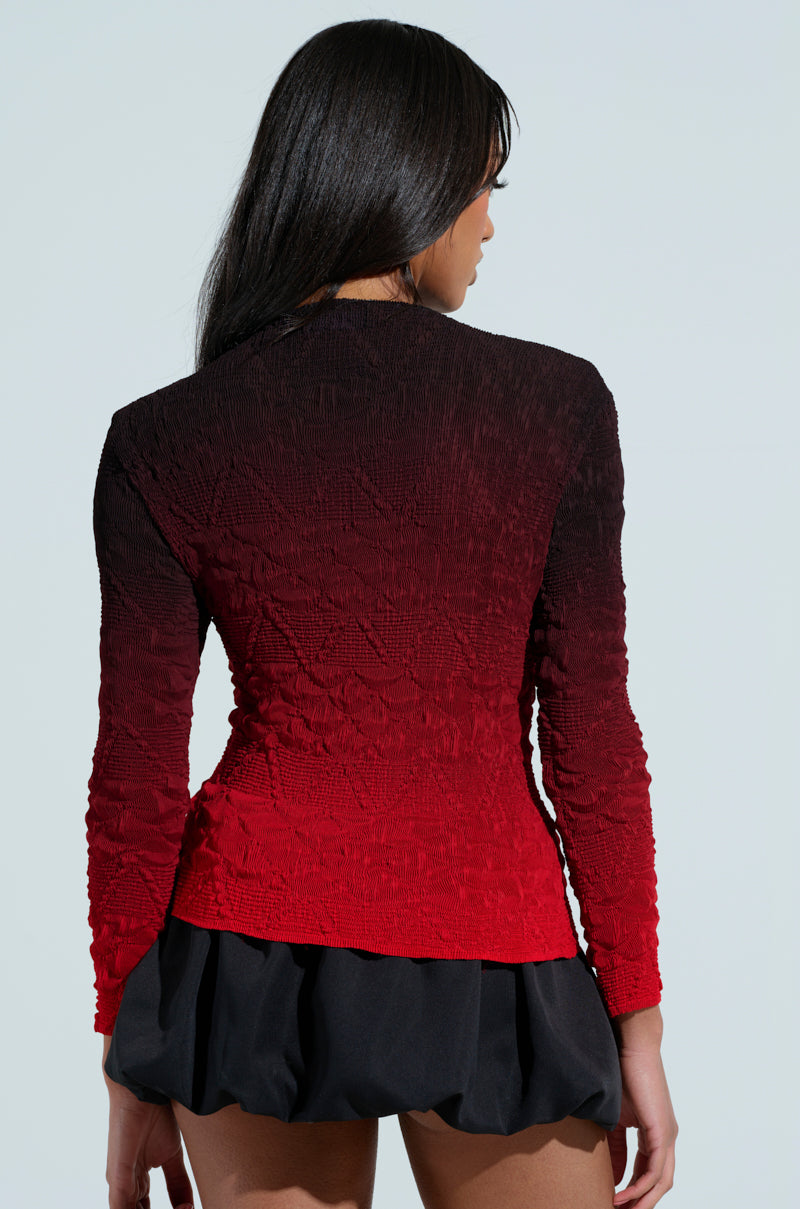 A person with long dark hair wears a BURNING PASSION TOP in red and black ombre paired with a black skirt. From the back, the curve-skimming silhouette of the top stands out against a plain background.