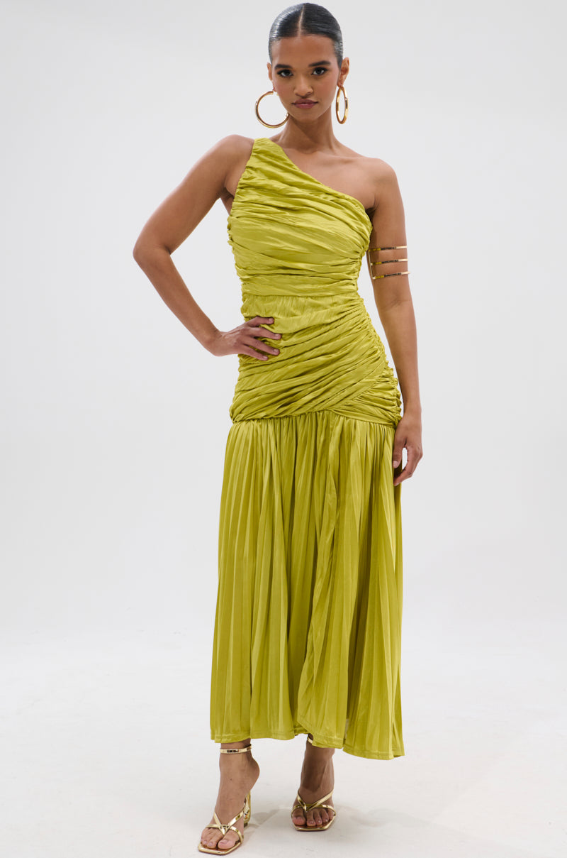 A woman poses against a plain white background in the LIFE OF THE PARTY SATIN MIDI DRESS, a bright yellow one-shoulder piece featuring a ruched satin midi skirt. She accessorizes with bold hoops, strappy heels, arm cuffs, and sleek hair.