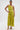 A woman poses against a plain white background in the LIFE OF THE PARTY SATIN MIDI DRESS, a bright yellow one-shoulder piece featuring a ruched satin midi skirt. She accessorizes with bold hoops, strappy heels, arm cuffs, and sleek hair.