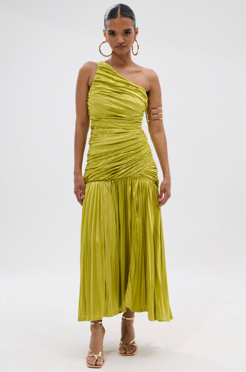 A woman faces forward in the LIFE OF THE PARTY SATIN MIDI DRESS, a shiny light green one-shoulder satin midi with a pleated skirt. She accessorizes with gold hoop earrings, an arm cuff, and gold heels, her hair pulled back against a neutral backdrop.
