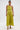 A woman faces forward in the LIFE OF THE PARTY SATIN MIDI DRESS, a shiny light green one-shoulder satin midi with a pleated skirt. She accessorizes with gold hoop earrings, an arm cuff, and gold heels, her hair pulled back against a neutral backdrop.