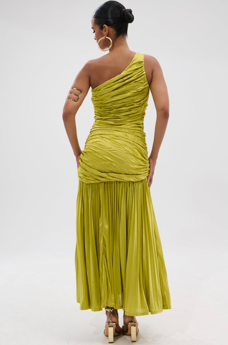 A woman stands facing away, wearing the LIFE OF THE PARTY SATIN MIDI DRESS in lime green with a ruched bodice and flowing skirt. She styles it with a bun, gold hoop earrings, an arm cuff, and high-heeled sandals against a plain background.
