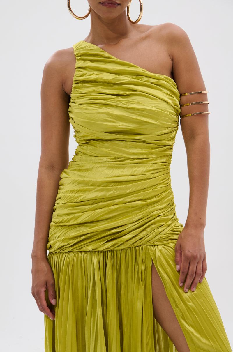 A woman wears the LIFE OF THE PARTY SATIN MIDI DRESS in lime green—one-shoulder, ruched, with a thigh-high slit—paired with gold hoop earrings and a gold cuff bracelet, standing against a plain white background.