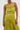 A woman wears the LIFE OF THE PARTY SATIN MIDI DRESS in lime green—one-shoulder, ruched, with a thigh-high slit—paired with gold hoop earrings and a gold cuff bracelet, standing against a plain white background.