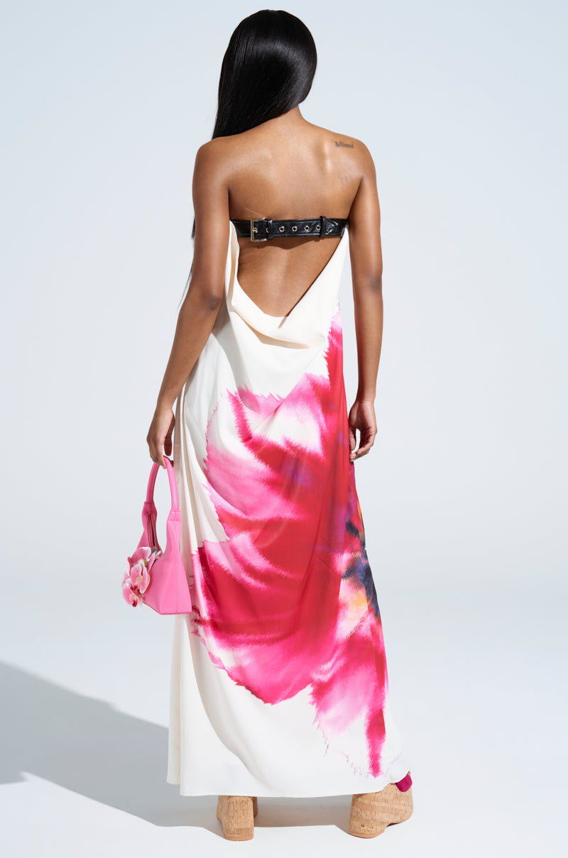 A woman faces away, showcasing the SWEET AND SPICY SATIN MAXI DRESS with a plunging cowl back and bold pink and red abstract florals. She pairs it with wedge sandals, a small pink handbag, and lets her long straight hair flow down her back.
