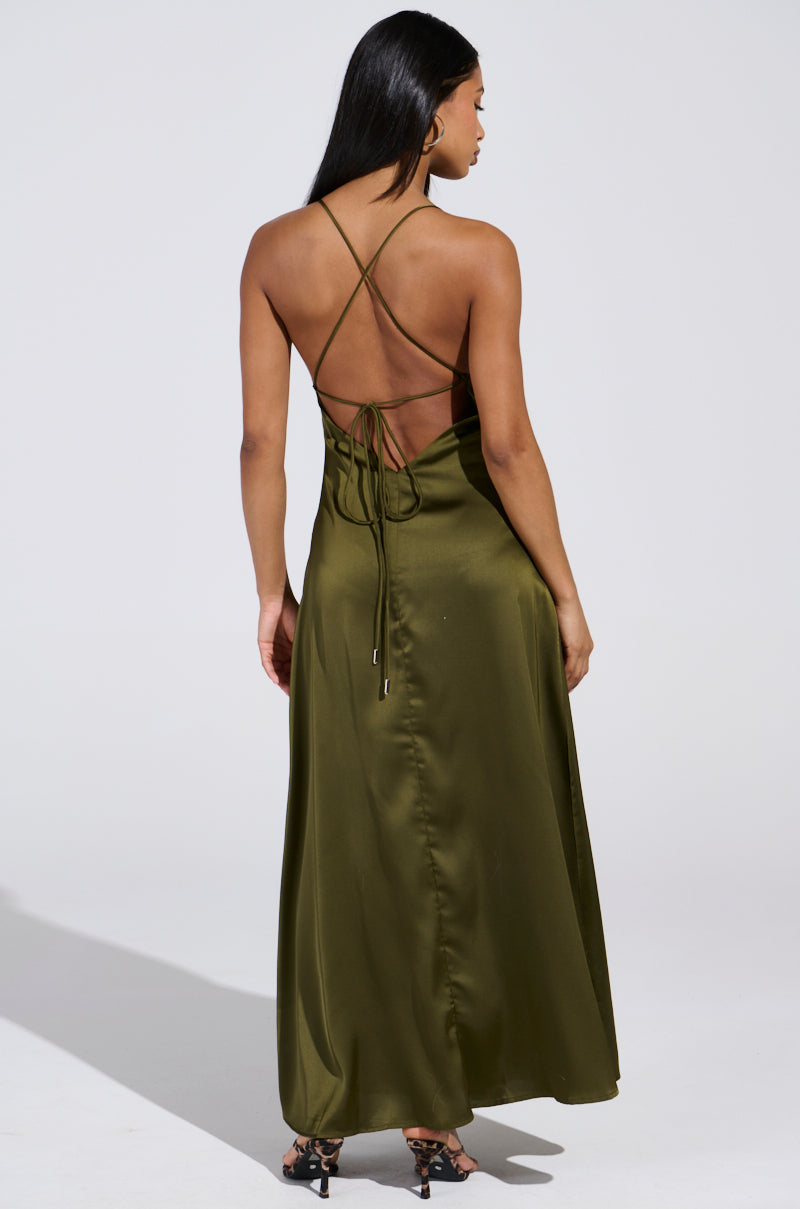 A woman with long dark hair wears the olive green STRAIGHT FROM THE 90'S SATIN MAXI DRESS, featuring a backless design, plunging neckline, and floor-length hem. She stands against a plain white background, highlighting the dress's elegance and flow.