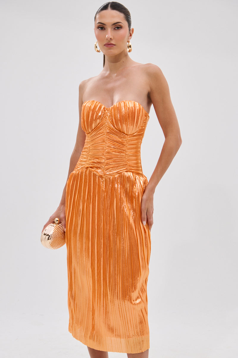 A woman wears the ALL ABOUT ME SATIN BUBBLE MIDI DRESS IN ORANGE, featuring shiny, strapless satin with a ruched, structured bodice. She holds a matching round clutch, stands against a plain background, and has her hair pulled back.