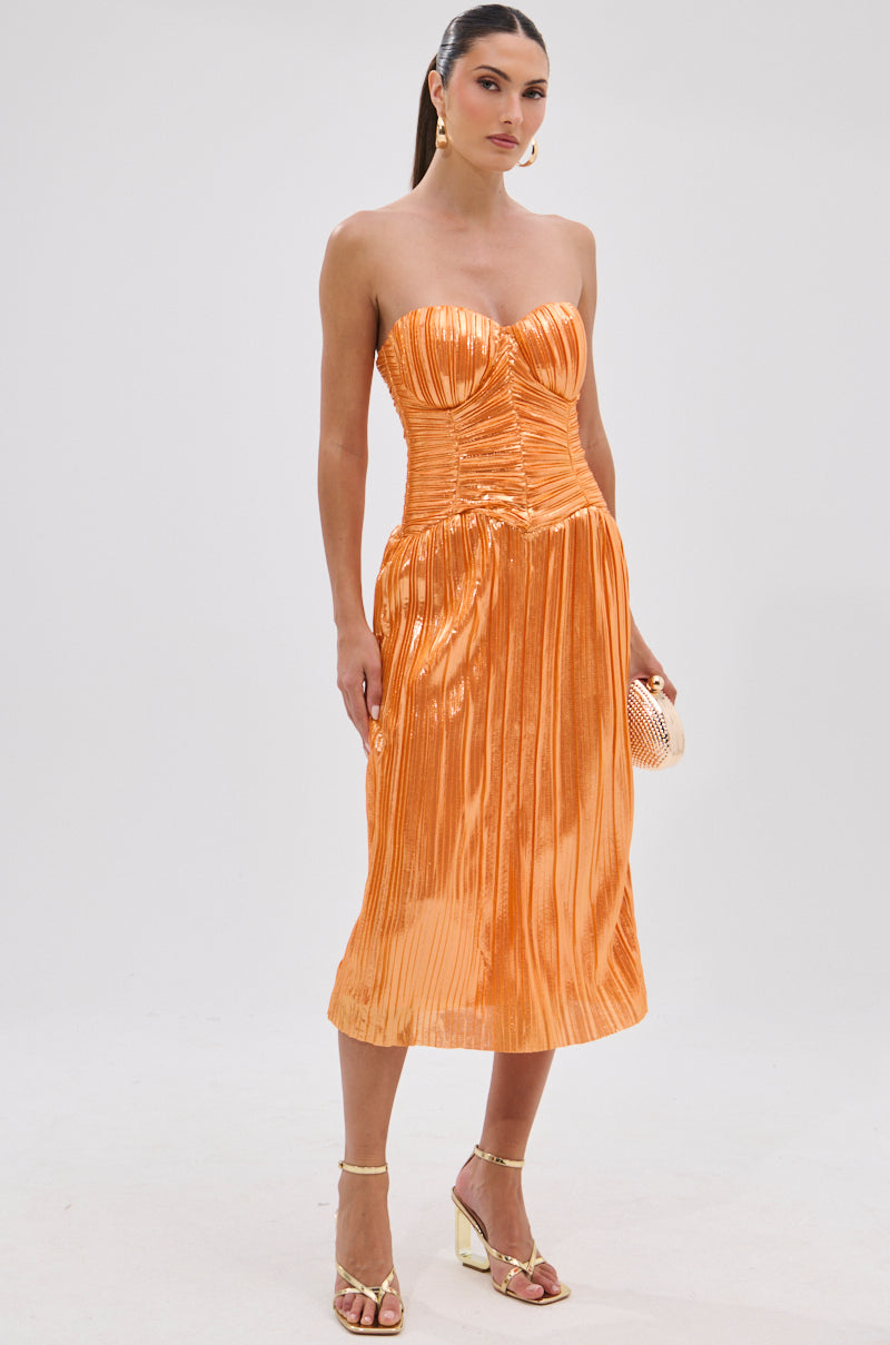 A woman models the ALL ABOUT ME SATIN BUBBLE MIDI DRESS IN ORANGE, styled with gold strappy heels, gold hoop earrings, and a textured clutch, standing against a plain white background.