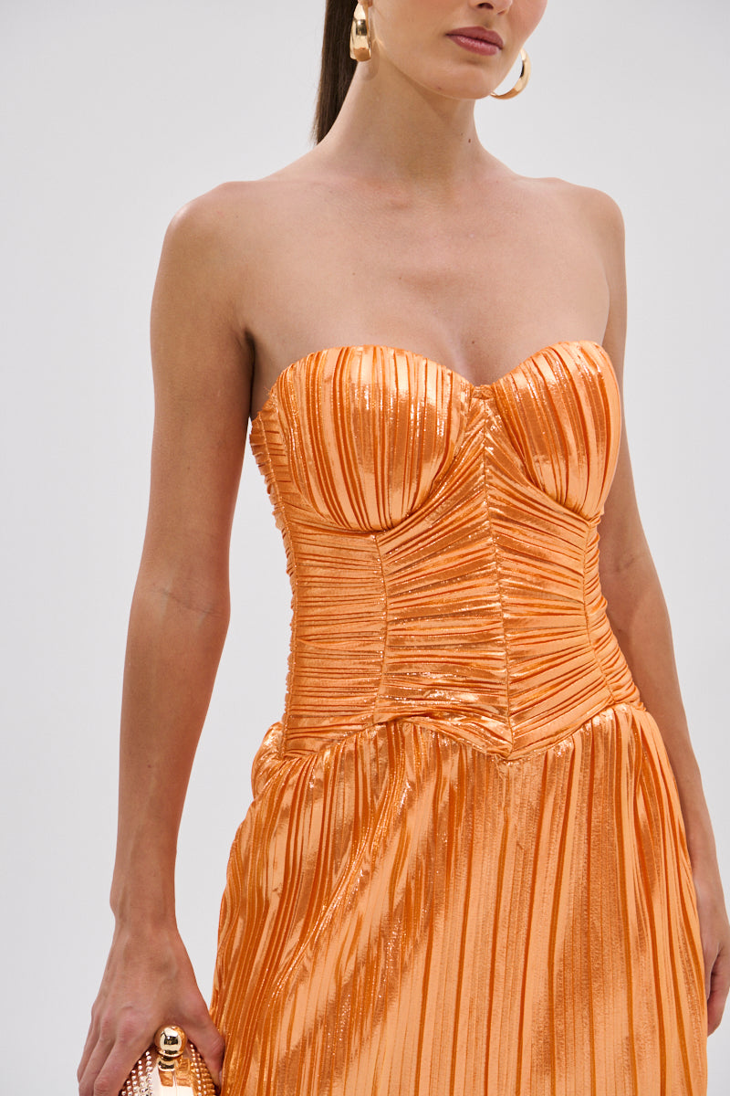 A woman wears the ALL ABOUT ME Satin Bubble Midi Dress in orange, featuring a strapless silhouette and metallic sheen. She holds a matching clutch, accessorizes with large gold hoops, and tucks her straight hair behind one ear.