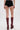 A person stands with their back to the camera, wearing TOO HOT TO HANDLE LACE HOT SHORT black shorts with a cheeky cut and tall, dark red platform boots against a plain white background.