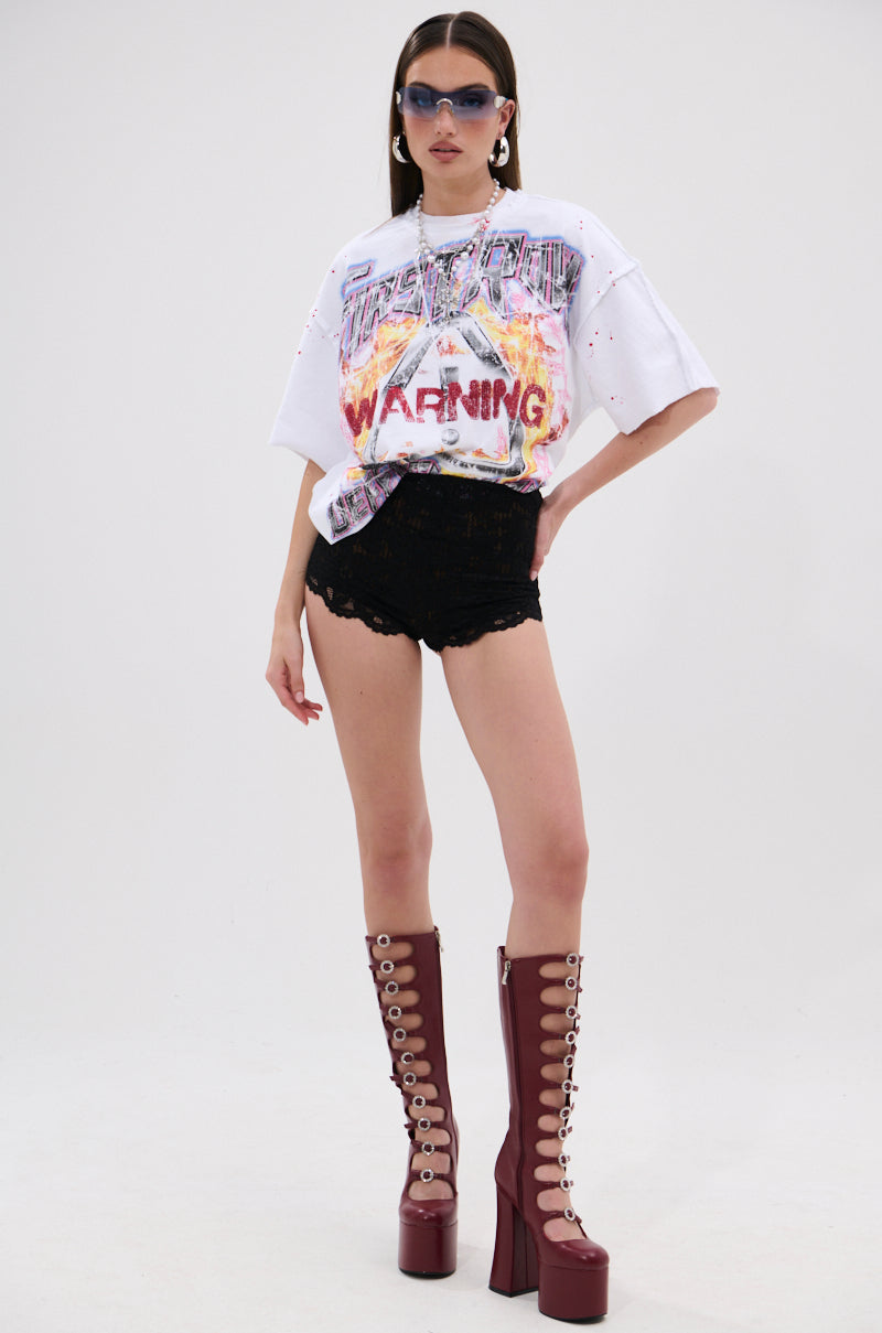 Wearing blue sunglasses, large earrings, a white "WARNING" graphic tee, TOO HOT TO HANDLE LACE HOT SHORT, and tall burgundy lace-up platform boots, a person poses confidently against a plain background. 6