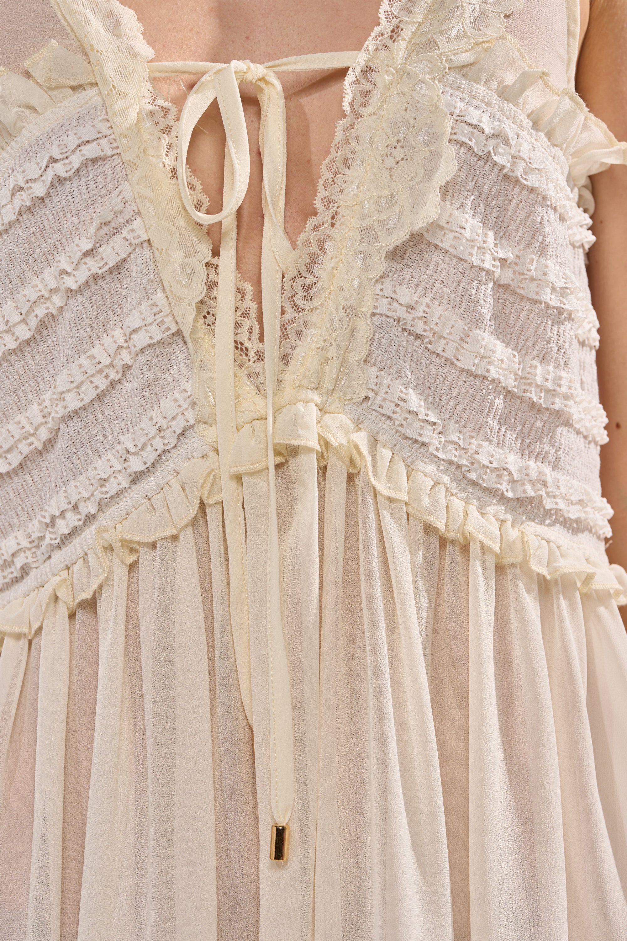 Close-up of the FREE SPIRIT LACE MINI DRESS—an ivory, cream lace-trimmed sheer dress with ruffled and gathered details, a deep V-neckline tied with a delicate ribbon; perfect for boho summer style. 5