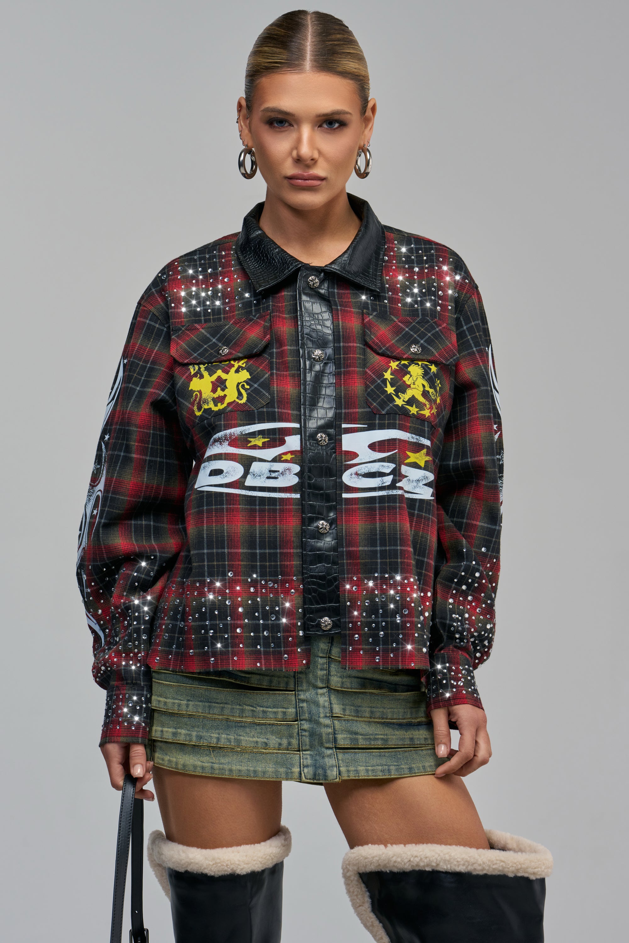 The CALL ME CRAZY RHINESTONE PLAID BUTTON DOWN is a red plaid shirt featuring rhinestone embellishments, crest-style patches, and a black croc faux leather collar and placket.