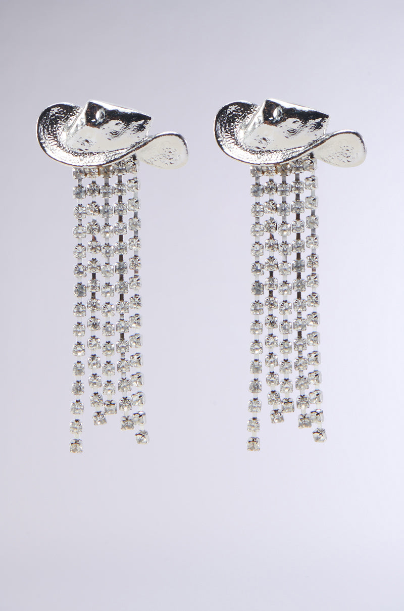 The GIDDY UP EARRING features intricate designs at the top, resembling a pair of dangling cowboy hats. Multiple rows of sparkling rhinestone fringe cascade downwards, creating a glamorous and elegant look against a plain background.