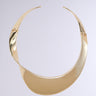 The TOP TIER CHOKER NECKLACE is a sleek, curved faux gold choker with a reflective surface. Its design showcases an asymmetrical, fluid shape that delicately twists around the neck. This piece of statement jewelry embodies a minimalistic and elegant appearance, creating a bold yet refined impression.