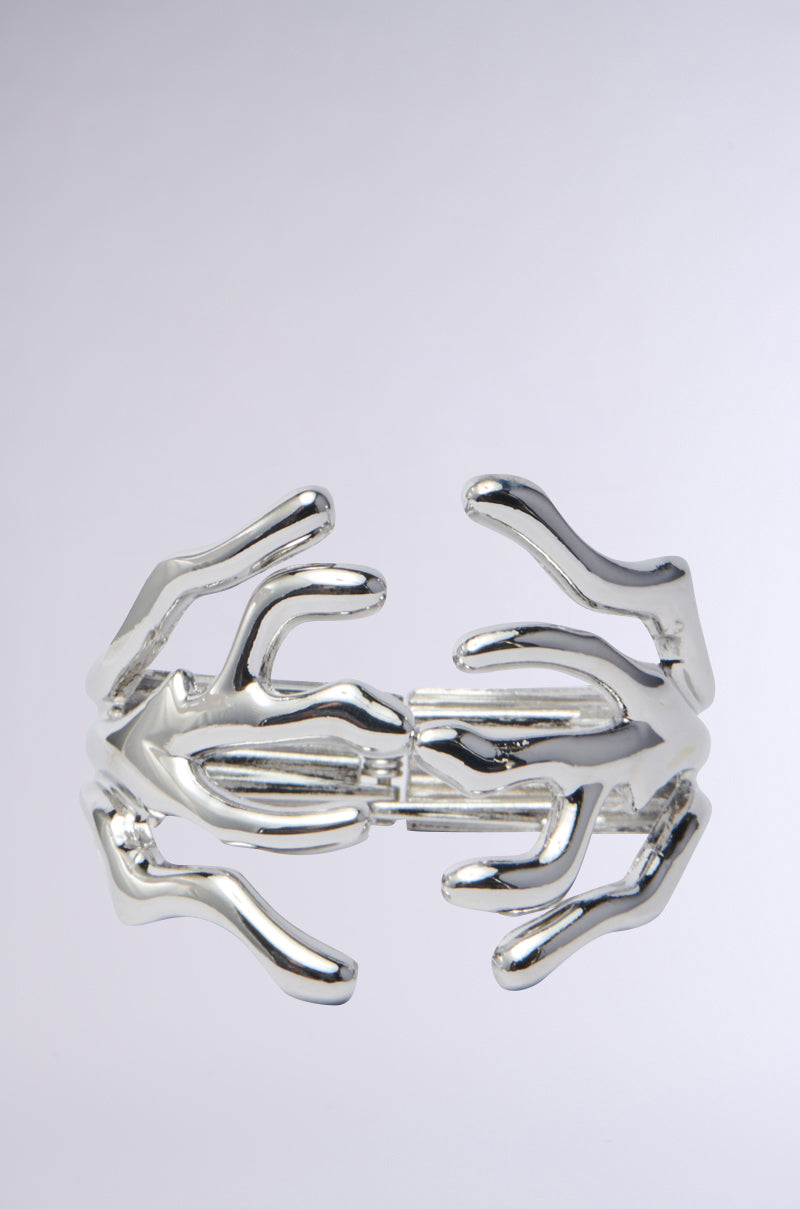 The CUFFED UP BRACELET IN SILVER features abstract, branch-like designs intertwining elegantly. This statement piece beautifully reflects light, accentuating its smooth and modern aesthetic against a plain backdrop.