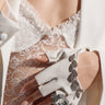 A person wears the IN THE ESTATE RING, featuring long manicured nails, fingerless white gloves, a white lace top, and a white blazer with pavé rhinestone trim.