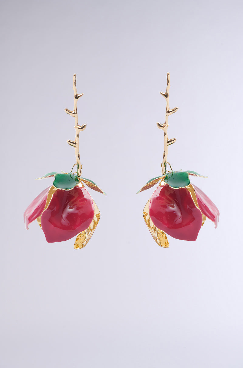 Meet the IN BLOOM EARRING: gold earrings with red floral pendants and green leaves in a branch-like design. The faux gold metallic base offers sophistication, while the floral silhouette adds natural elegance to any backdrop. 1