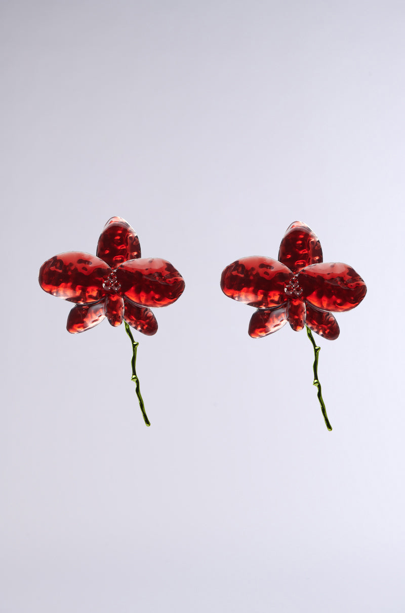 The BLOSSOM BEAUTY EARRING features two glossy red glass flower sculptures with delicate petals and rhinestone centers, resembling exquisite floral accessories against a plain light gray background. 0