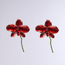 The BLOSSOM BEAUTY EARRING features two glossy red glass flower sculptures with delicate petals and rhinestone centers, resembling exquisite floral accessories against a plain light gray background.