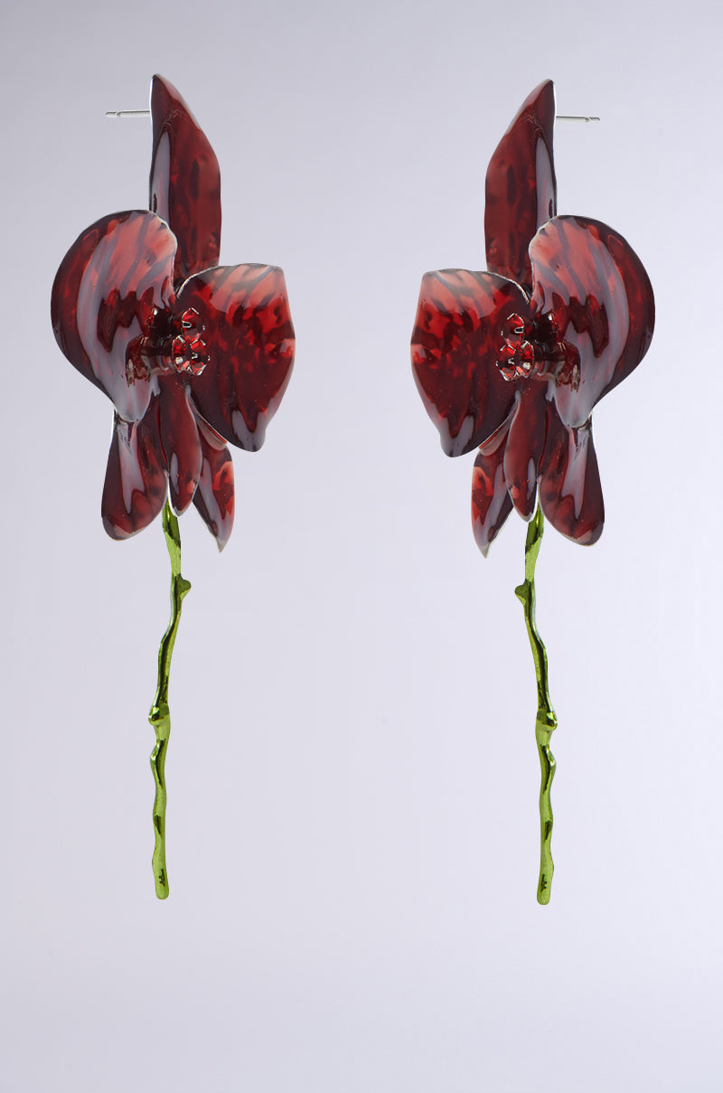 The BLOSSOM BEAUTY EARRINGS are ruby red with orchid shapes featuring glossy, textured petals and long green stems. They sparkle with elegant rhinestone centers and hang gracefully against a light gray background. 2