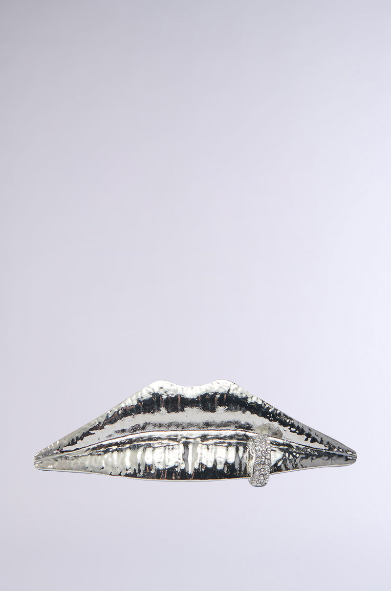 The LIP SERVICE RING features a metallic sculpture of lips with a finger gesture suggesting silence. Its textured, faux silver metallic surface stands out against a plain light gray background.