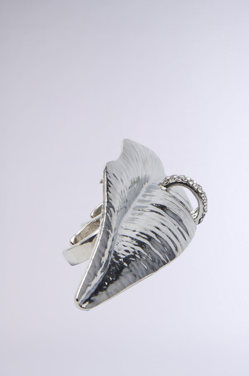 Introducing the LIP SERVICE RING: a faux silver metallic masterpiece resembling a detailed leaf with textured lines, featuring a small loop on one side. Set against a plain light gray background, it adds an elegant and intricate touch to any accessory collection.