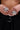 Close-up of two hands adorned with the IN THE SUN RING SET, each silver ring featuring pointed petal designs. The hands rest against a black outfit with a metal ring belt, highlighting the statement flower pendants.