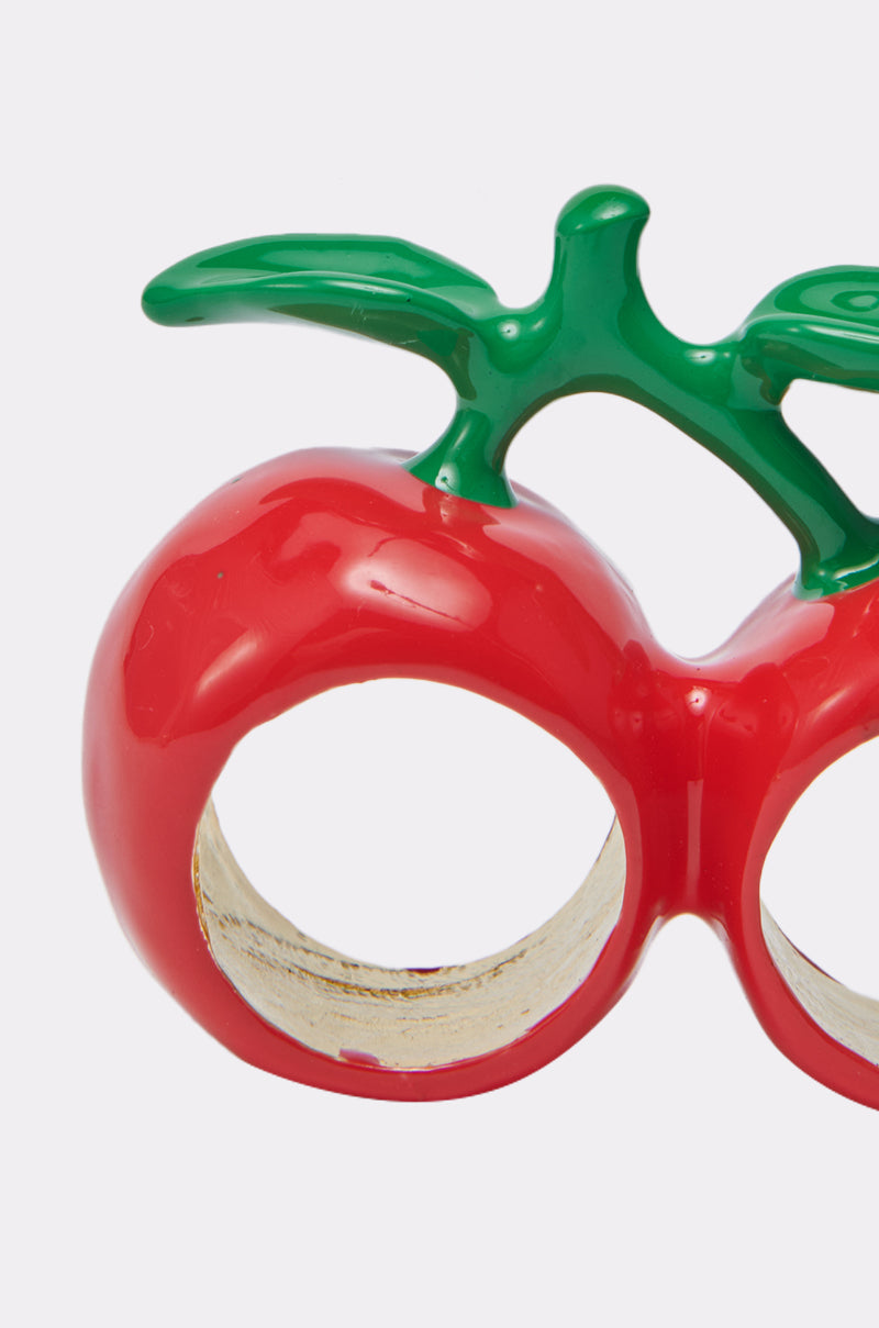 A close-up of the CHERRY BOMB RING, a shiny red double-finger ring with two circular holes and a green stem on top, displayed against a plain white background.