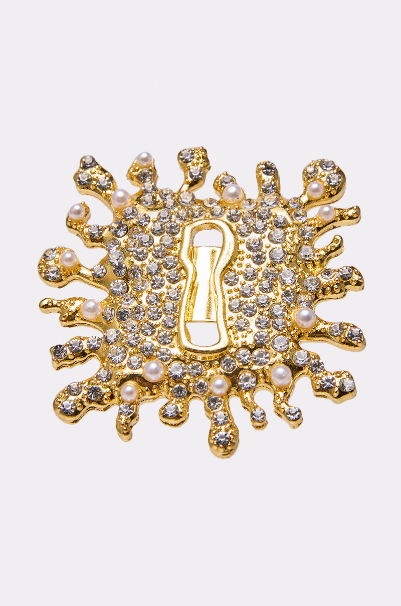 The UNLOCK ME RING is a gold ring with an irregular splatter design, clear gemstones and pearls, and a central keyhole-shaped cutout. 0
