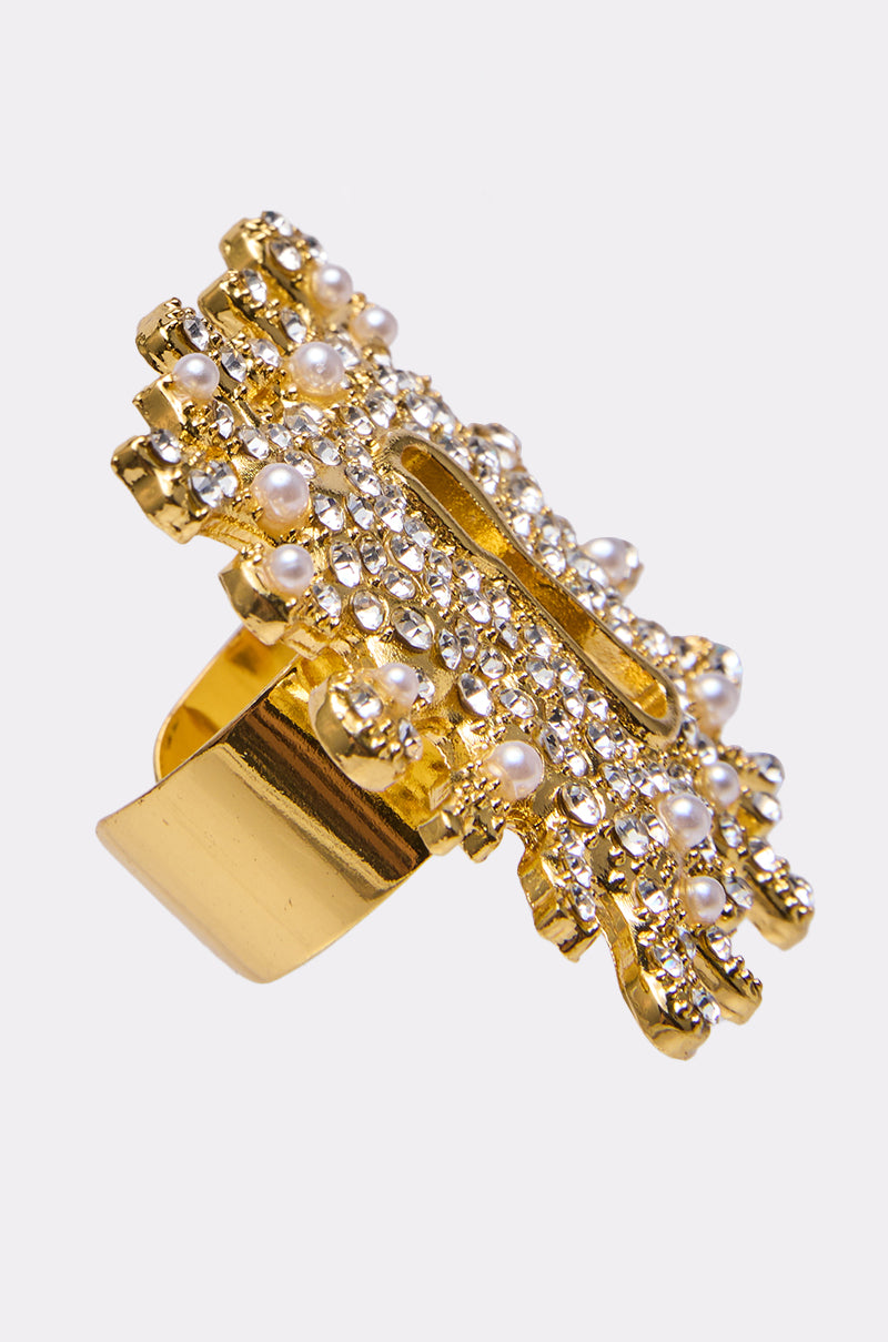 The UNLOCK ME RING is a gold statement piece adorned with sparkling white crystals and small pearls, featuring an ornate design and a wide, shiny band. 2