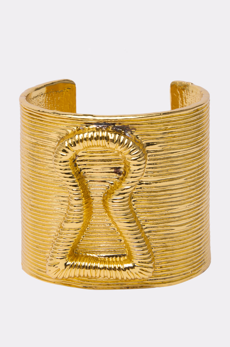 The IM THE KEY BRACELET is a wide, textured gold cuff with a raised keyhole design on the front, displayed against a simple light background.