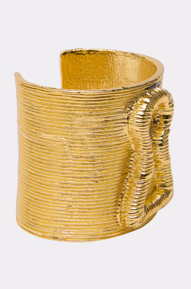 The IM THE KEY BRACELET is a wide, textured gold cuff featuring a wavy, looped design on one side, making it a striking statement piece that stands out against a plain light background. 6