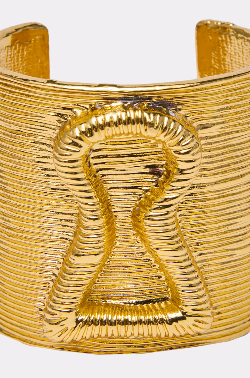 IM THE KEY BRACELET is a gold cuff with textured horizontal lines and a raised keyhole centerpiece—ideal for fans of keylock-inspired jewelry.