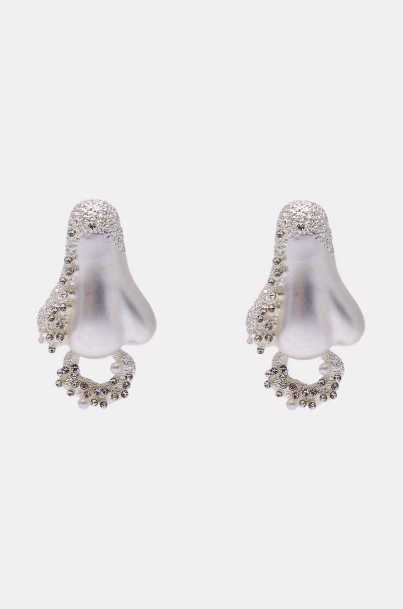 The SMELLS LIKE FASHION EARRING is a pair of silver statement earrings shaped like human noses, featuring small sparkling crystals along the edges and lower curves, displayed on a plain white background. 2