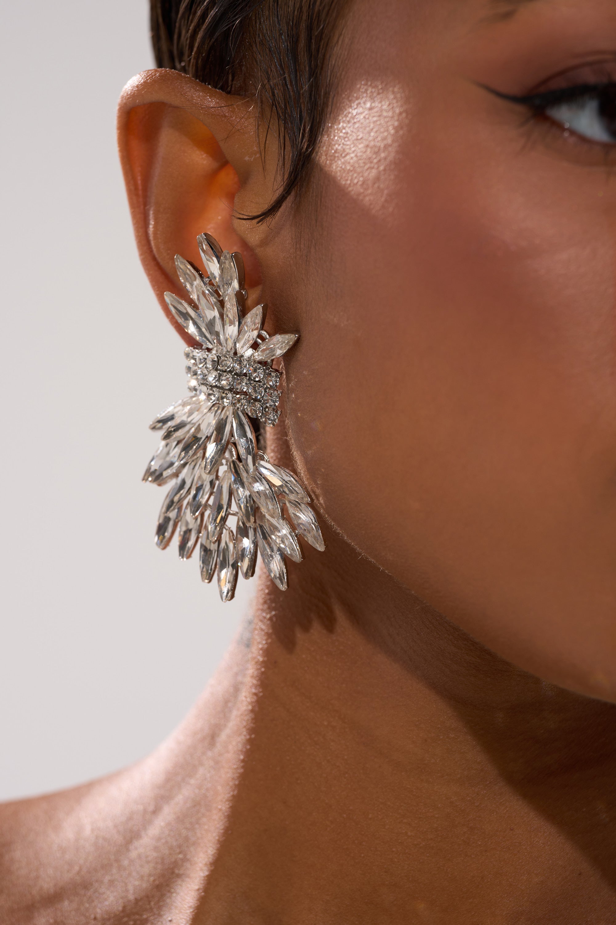 Close-up of a person’s ear wearing the CICI EARRING—a large, silver statement piece featuring multiple marquise-shaped crystals in a fan-like design, shown against a neutral background.