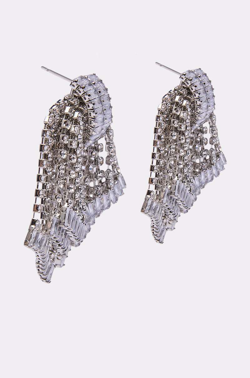 The ELI EARRING is a pair of silver chandelier-style statement earrings featuring sparkling rhinestones and multiple dangling strands, showcased against a plain white background.
