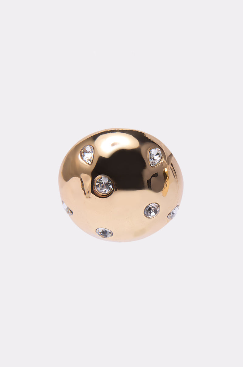 The PARI EARRING is a shiny, gold dome-shaped earring with several embedded round clear gemstones, reminiscent of statement jewelry, displayed on a plain white background.