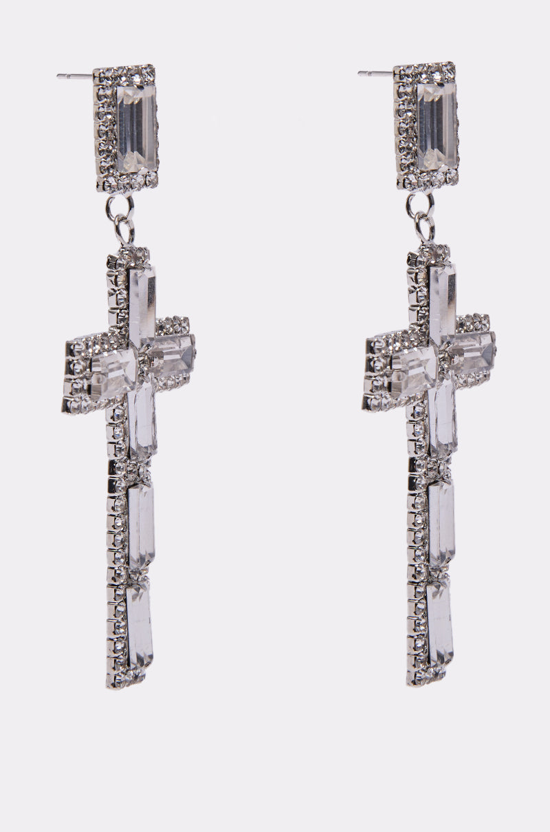 The RED CARPET EARRING is a pair of silver dangle earrings with cross designs, featuring rectangular and small round clear rhinestones, evoking glamorous style, shown against a plain white background. 2