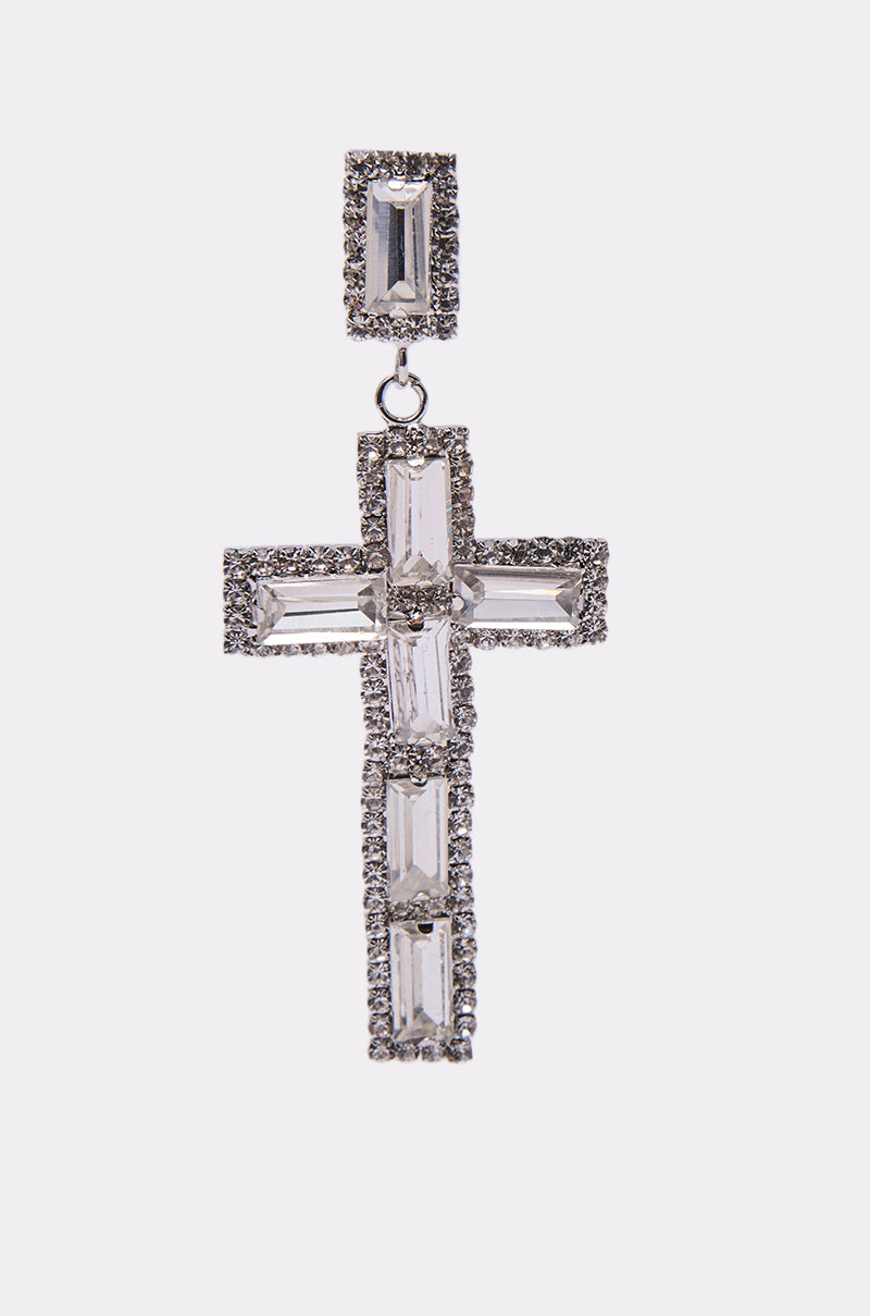 The RED CARPET EARRING showcases a dangling cross-shaped pendant with rectangular clear gemstones bordered by small round stones, all set in silver metal against a white background. 3