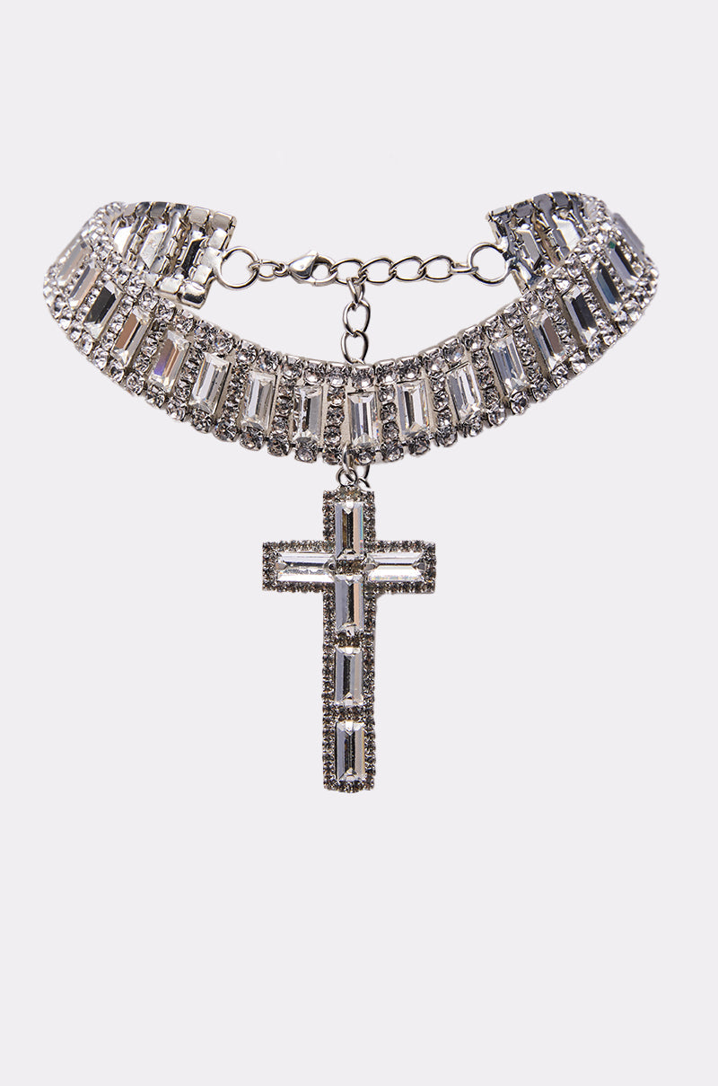 The CORY CROSS NECKLACE is a crystal choker with rectangular baguette rhinestones and a large cross pendant embellished with clear stones, shown on a plain white background. 0