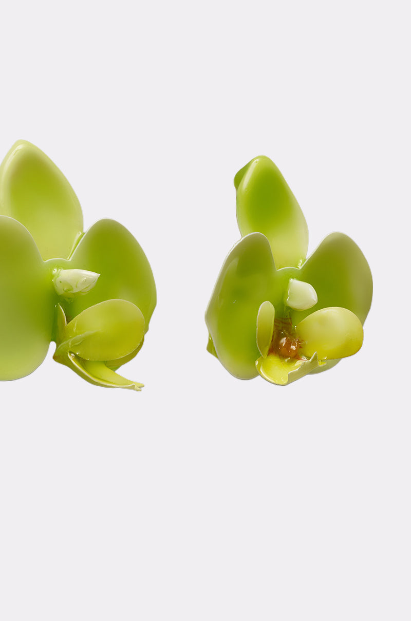 Close-up of two glossy, green TAKE ME OUT EARRING pieces inspired by orchids, featuring thick, shiny petals. The right earring shows a vibrant yellow-orange center, all set against a plain white background. 5