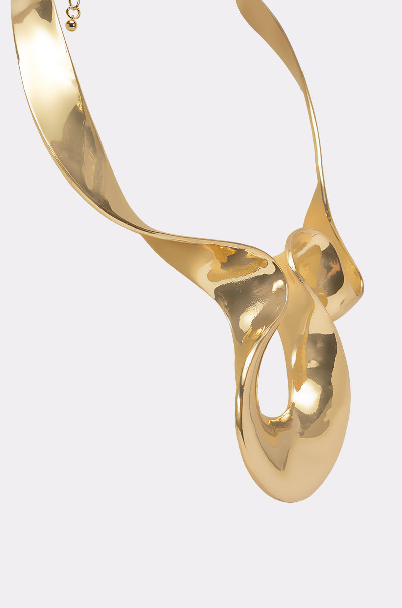 The PURE VIBES NECKLACE is a sculptural collar with a shiny gold, twisted abstract loop design and high-polish finish, creating a bold statement against a plain white background. 3