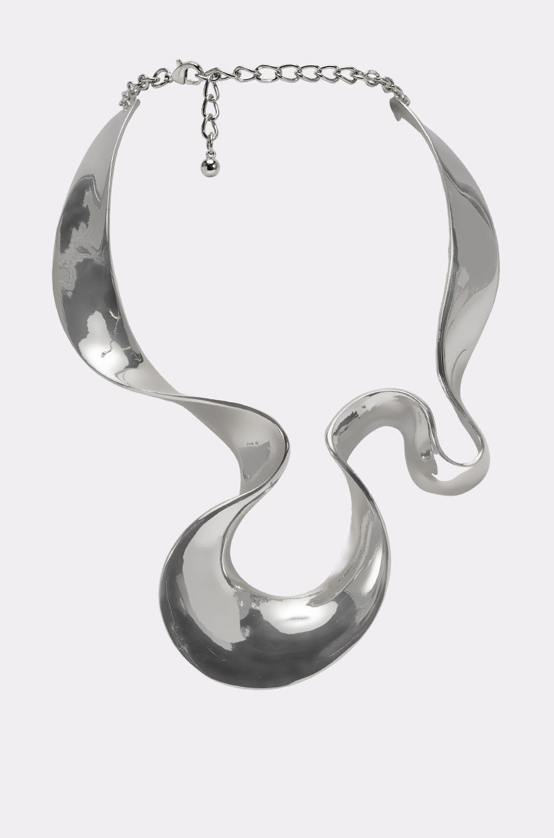 The MOLTEN DREAMS NECKLACE features a sculptural, wavy design with shiny, curved silver surfaces and a chain clasp—an artistic statement piece that adds a modern finishing touch to any look. 0