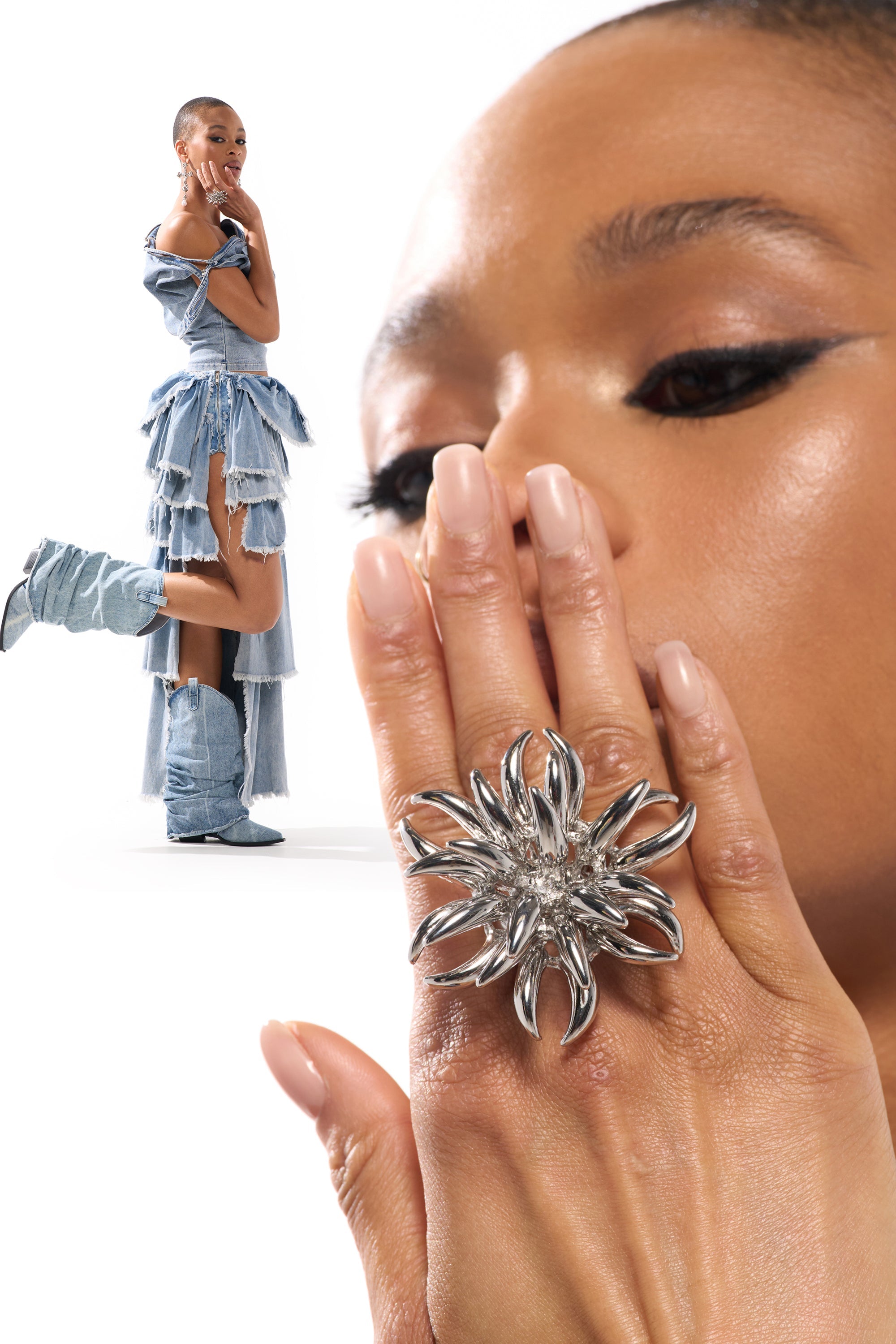 A woman in layered denim and boots poses with arms crossed. In the foreground, her hand wearing the JENNY SILVER RING partially covers her face, highlighting bold eye makeup and glossy lips against a white background. 0