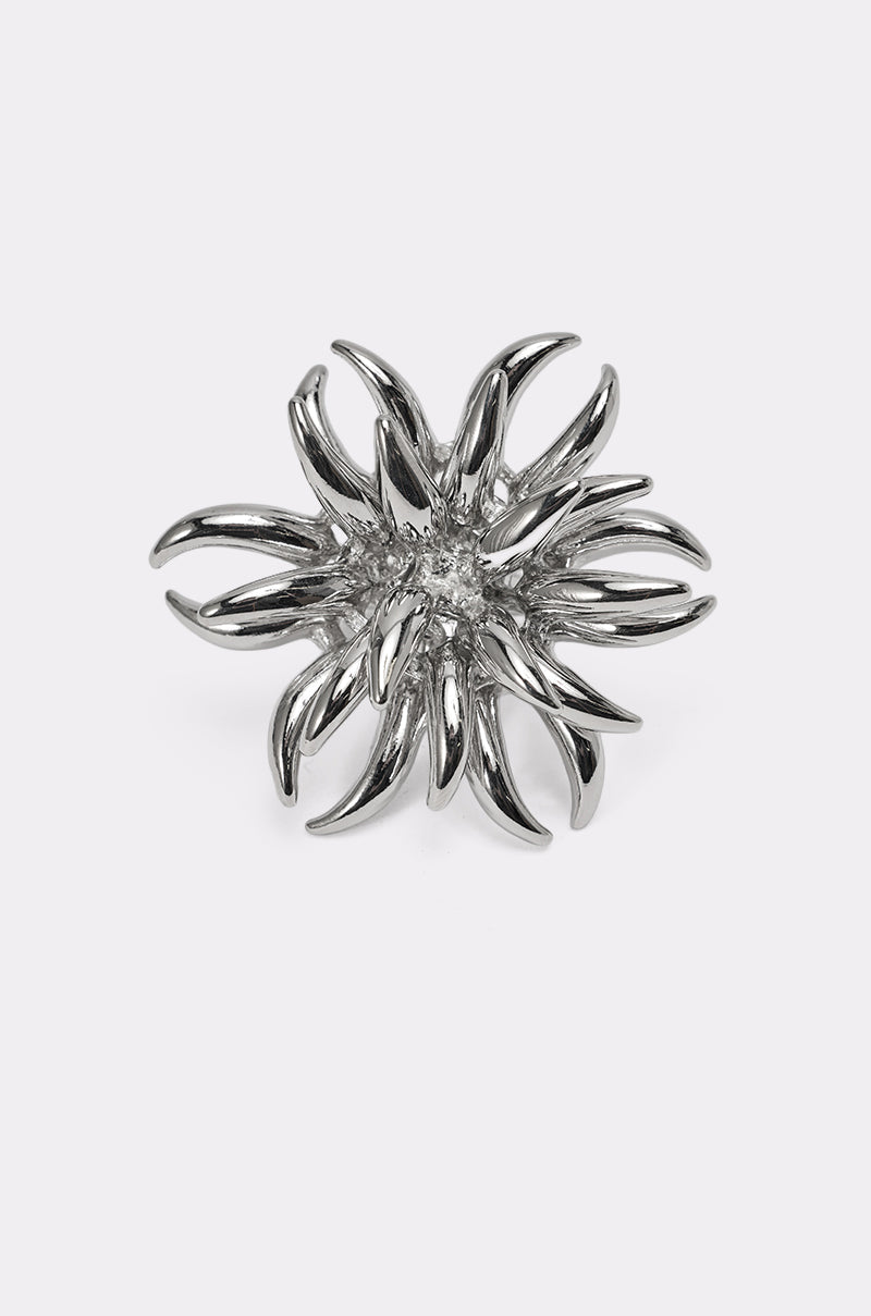 The JENNY SILVER RING features silver, curved spikes that evoke a blooming flower or sea anemone, making it a striking statement piece that stands out beautifully against a plain white background. 2