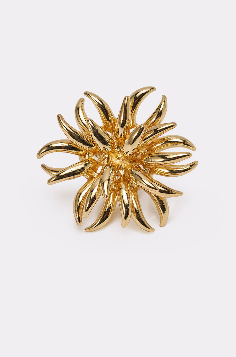 The SUNBURST GOLD RING features bold gold spikes in an abstract flower or starburst design, shown on a plain white background. 1