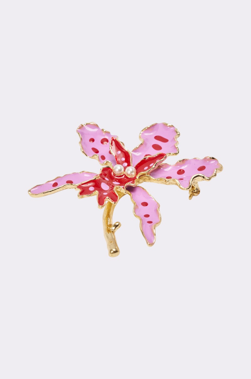 The EPITOME OF BEAUTY BROOCH is a gold floral enamel pin with five pink and red petals, pearl-like beads in the center, set against a light purple background—an elegant accessory inspired by delicate blooms. 2